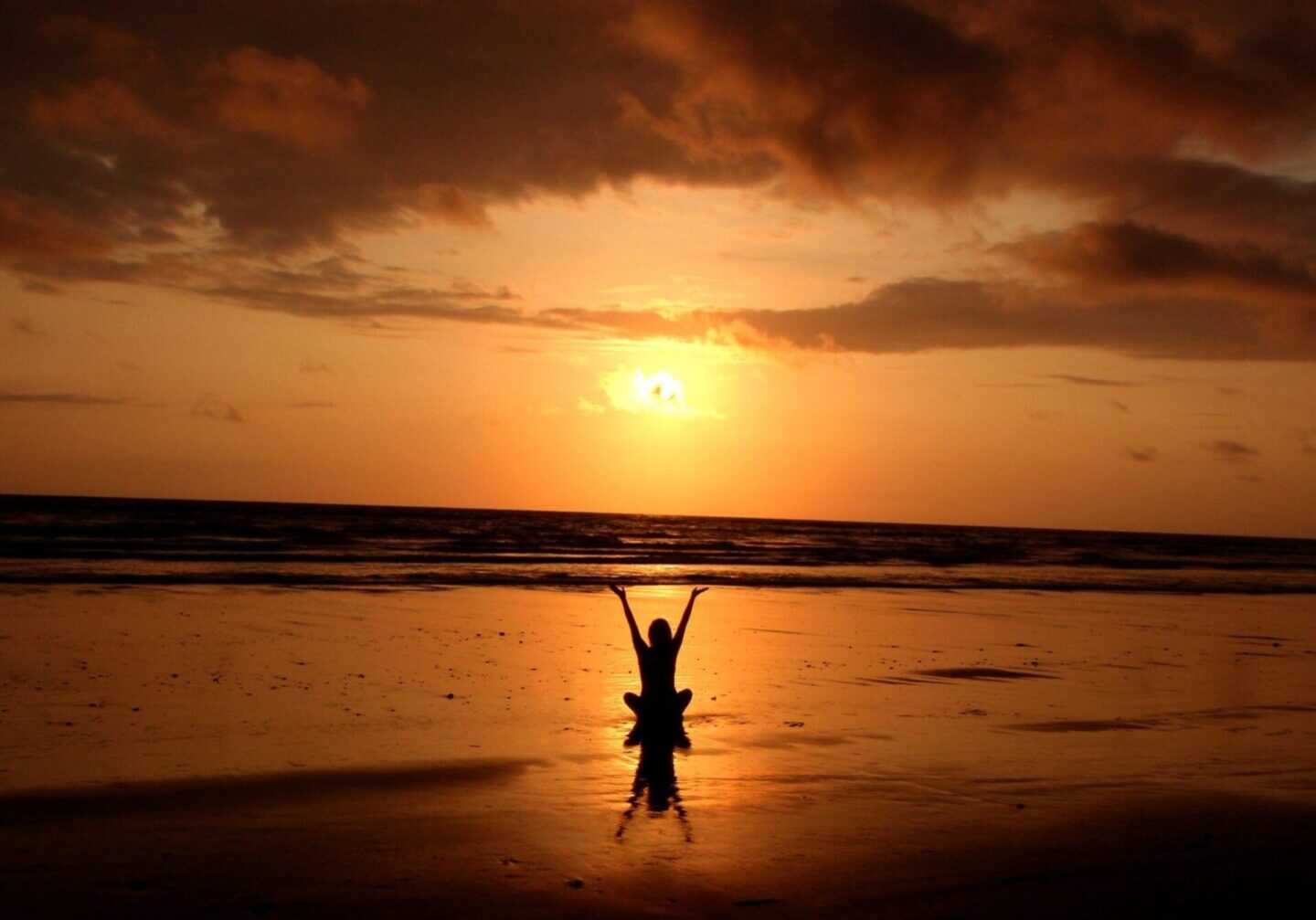 Person joyfully raising arms at sunset on a reflective beach. Person joyfully raising arms at sunset on a reflective beach.